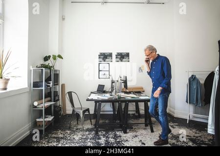 Smiling senior craftsman talking on smart phone in office Stock Photo