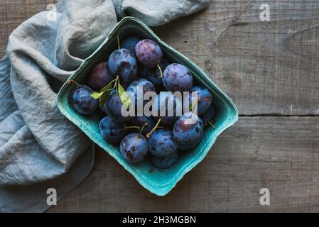 Top view of carton of fresh picked plums on wooden background. Stock Photo