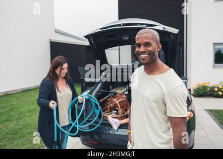 Portrait of smiling man with woman rolling cable by electric car Stock Photo