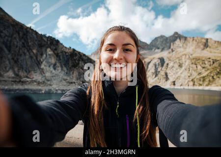 Girl taking a selfie while smiling with a lake in the background Stock Photo