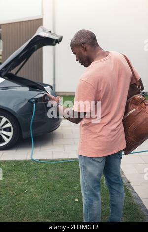 Rear view of man using smart phone while standing with backpack at charging station Stock Photo