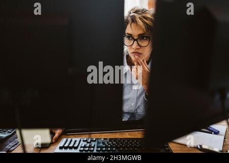 Serious businesswoman seen through computer monitor sitting at desk Stock Photo