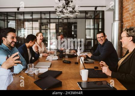 Cheerful business professionals laughing while sitting at conference table in board room Stock Photo