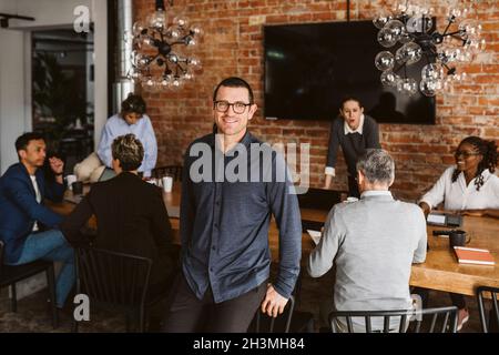 Portrait of smiling businessman standing while colleagues discussing in background Stock Photo