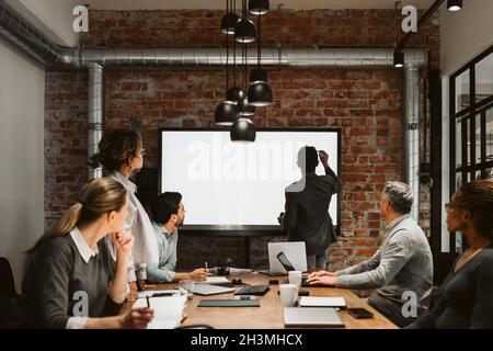 Male and female entrepreneurs looking at businessman writing on projection screen Stock Photo