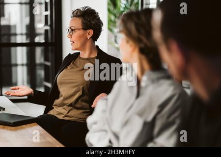 Mature businesswoman brainstorming colleagues while sitting in board room Stock Photo