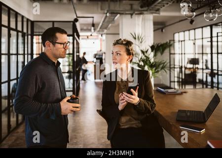 Mature businesswoman discussing over phone with male coworker in office Stock Photo