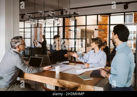Female entrepreneurs discussing while sitting with male colleagues at desk in creative office Stock Photo