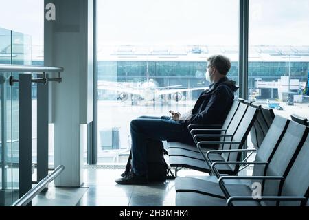 LONDON, UNITED KINGDOM - Sep 29, 2021: A male with a protective mask sitting alone at the airport with an airplane behind in London, UK Stock Photo