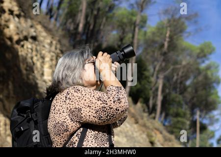 older white-haired woman taking pictures in the forest Stock Photo