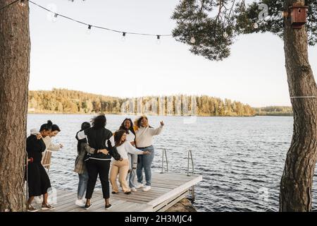 Young female friends dancing on jetty over lake Stock Photo