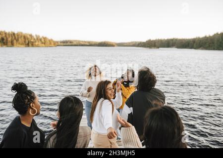 Happy female friends dancing at lakeshore against clear sky Stock Photo