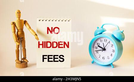 Wooden doll stands near a notepad with the text, No Hidden Fees, near an alarm clock on a white background Stock Photo