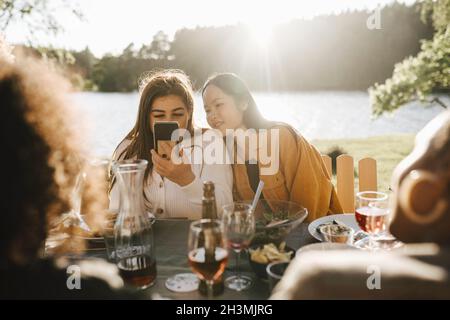 Young woman using smart phone while sitting with female friends at party Stock Photo