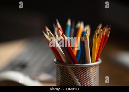 Office workplace. Focus on multi-colored pencils in foreground at wooden table with laptop computer on it. Copty space for text Stock Photo