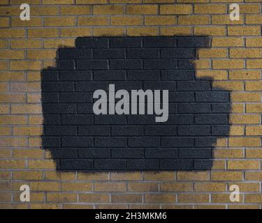 October 2021 - Blank yellow brick wall with a black painted patch covering graffiti Stock Photo