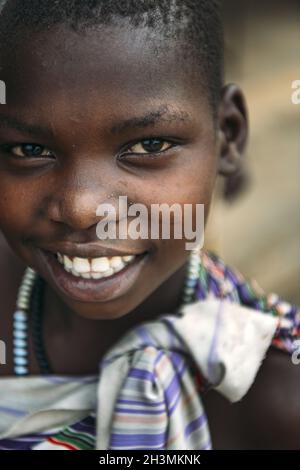 TOPOSA TRIBE, SOUTH SUDAN - MARCH 12, 2020: Girl in colorful garment with beads smiling and looking at camera in village of Topo Stock Photo