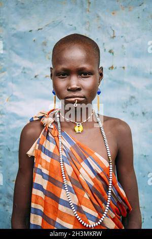 TOPOSA TRIBE, SOUTH SUDAN - MARCH 12, 2020: Girl in checkered colorful garment and with traditional accessories looking at camer Stock Photo