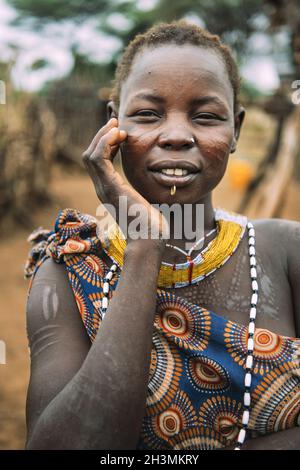 TOPOSA TRIBE, SOUTH SUDAN - MARCH 12, 2020: Young woman with traditional scars of Toposa Tribe touching face and looking at came Stock Photo