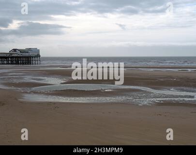 View of the south pier in blackpool with the beach at low tide in front of the sea and a cloudy sky Stock Photo