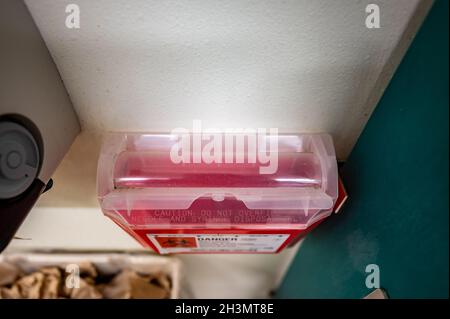 Red biohazard sharps waste container mounted to the wall of a public restroom Stock Photo