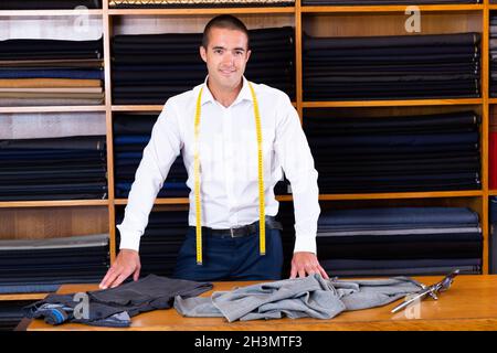 Portrait of concentrated young handsome tailor working in mens cloths store Stock Photo