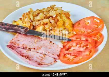 Rustic and simple breakfast of ham, potatoes, and tomato slices Stock Photo