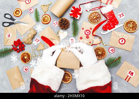 Santa Claus preparing the advent calendar. Eco craft envelopes with gifts for children. Seasonal Christmas tradition. Flat lay, top view. Stock Photo
