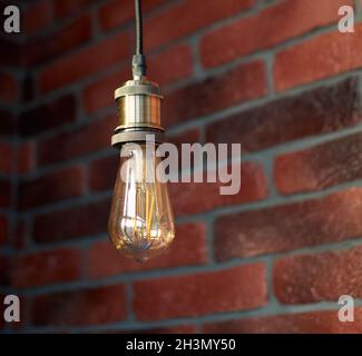Modern edison loft decorative lamp hanging from the ceiling. Fixture of lamp. Minimalist interior design. Stylish bedroom and livingroom. Red brick Stock Photo