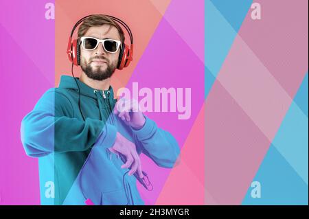 Funky young bearded hipster man in glasses and headphones dances and listens pleasurable music in his smartphone. love live. Lei Stock Photo