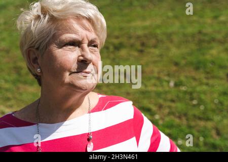 Serious mature woman portrait on stripes shirt on sunny day. Senior lady with concerned, worried look. Retirement, menopause, problem concepts Stock Photo