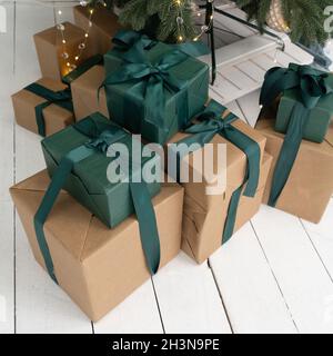 New Years presents lie under the Tree. Gifts in brown boxes and green packaging. Boxes decorated with ribbons and bows. Close up Stock Photo