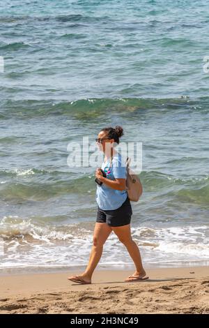 young woman walking alone along a sandy beach while on holiday on the greek ionian island of zakynthos, female walking on beach, lone woman on holiday Stock Photo