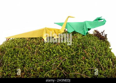 Group of colored origami paper dinosaurus on green moss isolated over white background Stock Photo