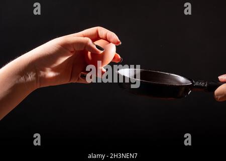 hand holding egg in front of frying pan. isolated on black background. Hand about to break an egg to throw it into frying pan. Stock Photo