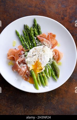 Eggs Benedict with parmesan, green asparagus and Parma ham. Stock Photo
