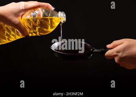 hand pouring vegetable oil on frying pan. isolated black background. yellow oil. Commercial kitchen concept. Stock Photo
