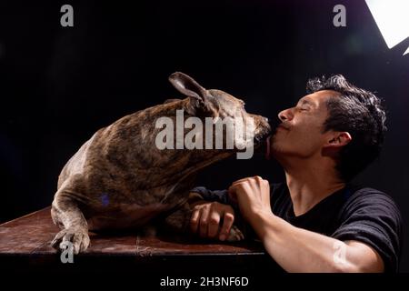 latin man gets licked by his dog. isolated on black background. Stock Photo