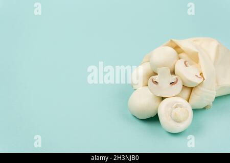 Champignon mushrooms in an eco-bag on a blue background with copy space. Side view Stock Photo