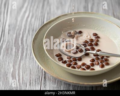 Dry breakfast. Milk splashing into spoon with chocolate cornballs over. Selective focus Stock Photo