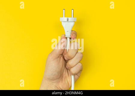 Hand with electrical power cable. Yellow background, flat lay, top view and copy space Stock Photo