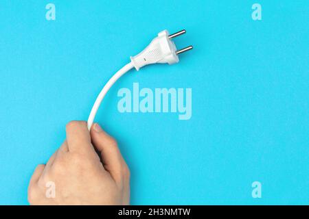 Hand holding power cable with EU plug on a bright blue background, flat lay, top view and copy space Stock Photo