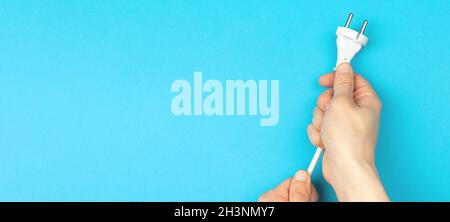 Hands holding power cable on a blue background, banner, flat lay, top view and copy space Stock Photo