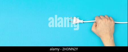 Banner, hand holding power cable with EU plug on a bright blue background, flat lay, top view and copy space Stock Photo