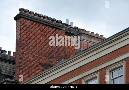 A large row of old fashioned traditional clay chimney pots on a red brick support against a grey sky from when buildings where b Stock Photo