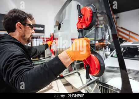 Automobile technician worker replacing windscreen or windshield of a car in auto service station garage. Stock Photo