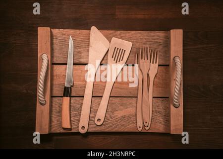 Wooden kitchen utensils laid out on wooden tray on wooden table horizontal banner. Top view Stock Photo
