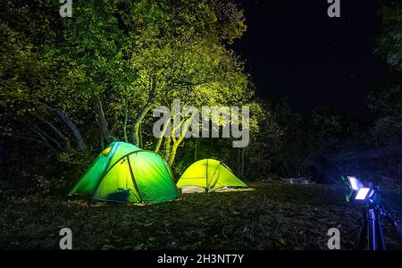 Tourist tents at night in woods. The lights are on in the tents. Stock Photo