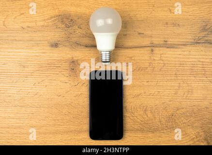 LED light bulb and mobile phone on a wooden table, top view Stock Photo