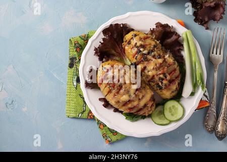 Baked potatoes stuffed with sausage and cheese on a white plate on blue background. Copy space Stock Photo